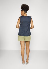 Top sem mangas azul-marinho com cintura franzida e alças de laço, combinado com calções texturizados verdes claros. Design simples e ajuste descontraído.