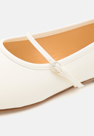 White synthetic flat shoe with a smooth finish, rounded toe, and a thin strap secured by a round buckle. Soft beige interior lining.
