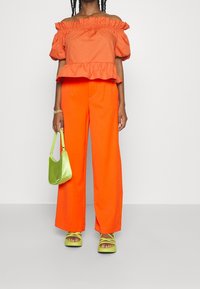 Orange off-shoulder ruffle topp, i kombination med klara orange vida byxor. Innehåller en grön väska och neongröna sandaletter med remmar.