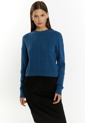 Blauwe kabelgebreide cropped trui met lange mouwen en ribgebreide manchetten, gecombineerd met een zwarte aansluitende rok met een gladde textuur.