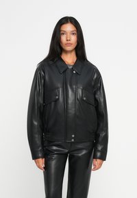 Veste en cuir noire avec un design à col, fermeture à boutons sur le devant, deux poches poitrine et des détails élastiques à la taille.