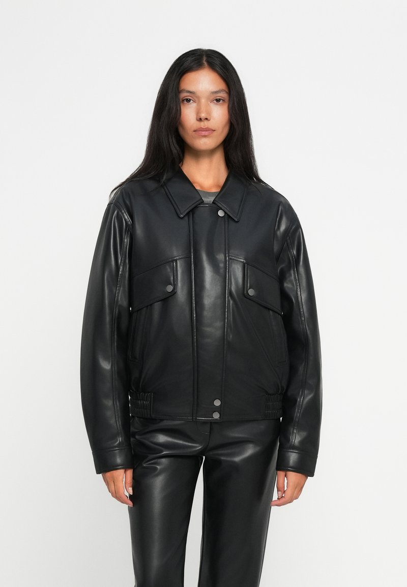 Veste en cuir noire avec un design à col, fermeture à boutons sur le devant, deux poches poitrine et des détails élastiques à la taille.