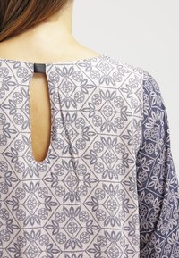 Blusa con tessuto stampato che presenta un motivo floreale in blu navy e bianco. Apertura a chiave sul retro con un piccolo anello di tessuto sul collo.