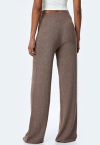 Pantalons marron à jambes larges en maille texturée. Le tissu présente un motif subtil, avec une taille haute et une coupe droite.