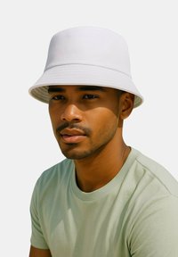 Weißer Bucket-Hut mit strukturiertem Design und breiter Krempe, aus einem strukturierten Stoff. Wird mit einem hellgrünen T-Shirt getragen.