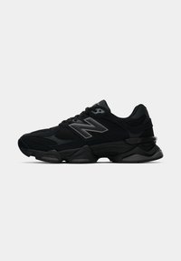 Chaussures de sport noires avec une tige en maille et synthétique, semelle épaisse, accents réfléchissants et un logo 'N' distinctif sur le côté.