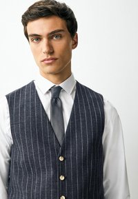 Navy striped waistcoat with vertical white lines, button front, paired with a white shirt and textured gray tie. Smooth fabric texture.