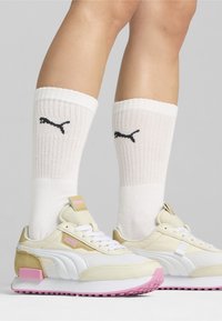 White and pink athletic shoes with textured leather and mesh, paired with ribbed white socks featuring black logo detail, worn above the ankle.