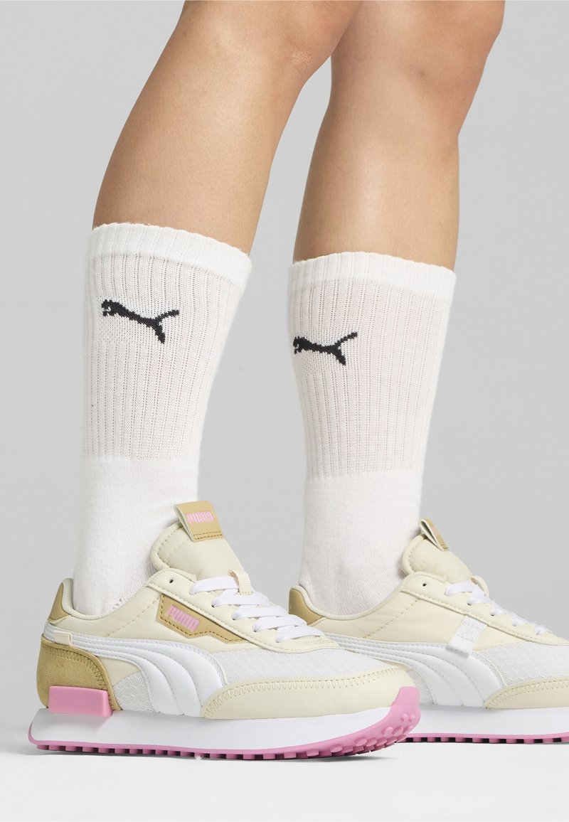 White and pink athletic shoes with textured leather and mesh, paired with ribbed white socks featuring black logo detail, worn above the ankle.