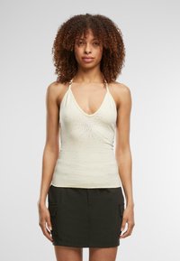 Lys beige halterneck top med dyb V-udskæring, der har et centralt dekorativt mønster med små rhinsten, parret med en mørk cargo nederdel.