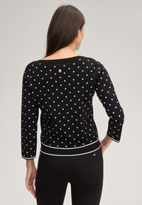 Μαύρο πουλόβερ με λευκές πουά βούλες, ριμπ ύφασμα στο λαιμό, μανίκια τριών τετάρτων και αντίθετη ταινία στη μέση. Χρυσή λεπτομέρεια με λογότυπο στο πίσω μέρος.