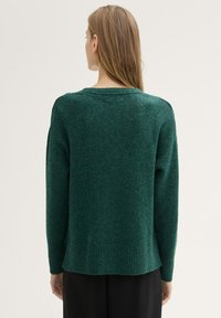 Pulover verde tricotat, cu o croială lejeră, tiv nervurat și fante laterale mici. Fabricat dintr-un material moale, cu un finisaj neted și texturat.