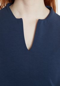 Haut bleu marine avec un décolleté en V, fabriqué dans un tissu lisse avec une texture subtile. Manches courtes et design simple.