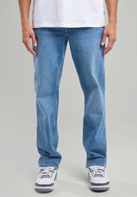 Jeans de denim azul claro con un corte recto, que presentan un diseño clásico de cinco bolsillos y un ligero desvanecimiento. Combinados con zapatillas blancas y grises.