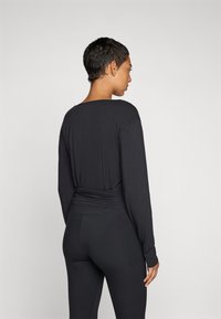 Fekete, hosszú ujjú, laza szabású top, kerek kivágással és rakott részletekkel a deréknál, fekete leggings-szel párosítva.