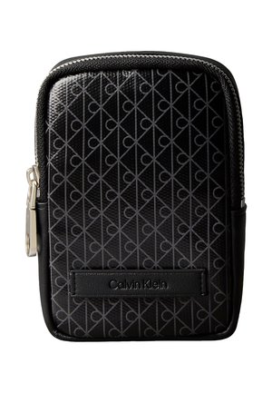 Bolsa negra con cremallera y superficie texturizada, que presenta un patrón geométrico y un logotipo prominente de Calvin Klein grabado en un parche de cuero.