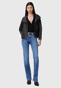 Zwarte leren jacket met een brede kraag, geribbelde zwarte top, blauwe flared jeans, slanke zilveren riem en zwarte puntige schoenen.