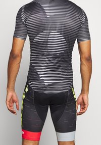 Černobílý pruhovaný cyklistický dres s krátkým rukávem, přiléhavý design. V kombinaci s černými šortkami s žlutými akcenty a červeným pruhem.