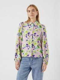 Blusa floral em rosa claro com padrões verdes e roxos, apresentando um colarinho, mangas bufantes e punhos elásticos. Combinada com jeans de ganga.