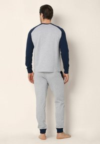 Pullover grigio in cotone con maniche lunghe blu navy e pantaloni grigi coordinati, con polsini e vita a costine. Modello scalzo di spalle.
