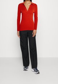Czerwony sweter z dzianiny z dekoltem w serek i kołnierzem, w połączeniu z czarnymi szerokimi spodniami i granatowymi trampkami z białymi akcentami.