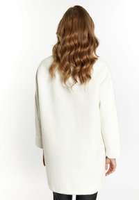 Witte textuurjack met een ontspannen pasvorm, lange mouwen en een afgeronde zoom, gezien van achteren, met los, golvend haar zichtbaar.