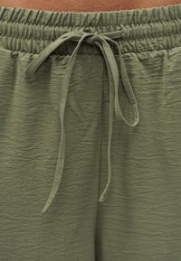 Παντελόνια από υφασμάτινο ύφασμα σε ελιά πράσινο με ελαστική μέση και δέσιμο κορδονιού στο κέντρο μπροστά.