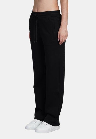 Zwarte trainingsbroek met een elastische tailleband, verstelbaar trekkoord en zijzakken, gecombineerd met witte sneakers. Soepele stoftextuur.