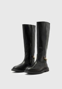Stivali neri in pelle al ginocchio con zip laterale, dettagli in metallo dorato e suola nera texturizzata. Design minimalista con una finitura liscia.