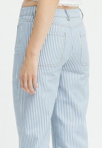 Ljusblå och vita randiga denimbyxor med hög midja, med bakfickor, en slät yta och synliga sömdetaljer.