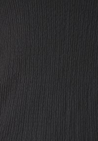 Tissu noir texturé présentant un motif côtelé avec des lignes verticales, créant un effet tridimensionnel subtil. Matière douce et légèrement extensible.