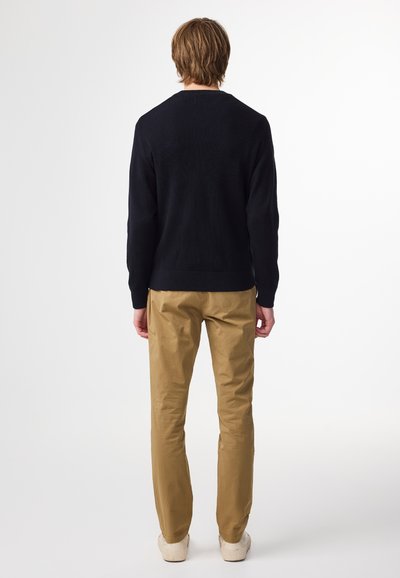 Mörkblå ribbade tröja med långa ärmar, i kombination med beige tapered byxor och off-white sneakers, sedd bakifrån.