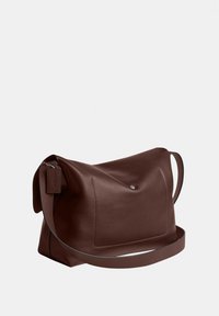 Sac à bandoulière en cuir marron foncé avec une poche avant, une sangle unique et un petit détail en métal sur un fond uni.