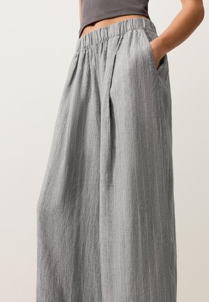 Pantaloni larghi in lino grigio con sottili righe verticali e vita elastica, indossati con una mano in tasca e un top corto.