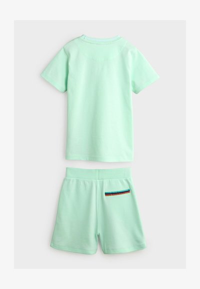 Mätovo zelené bavlnené tričko s krátkymi rukávmi a zodpovedajúce šortky, ktoré majú pruhovaný vreckový akcent na zadnej pravej strane šortiek.