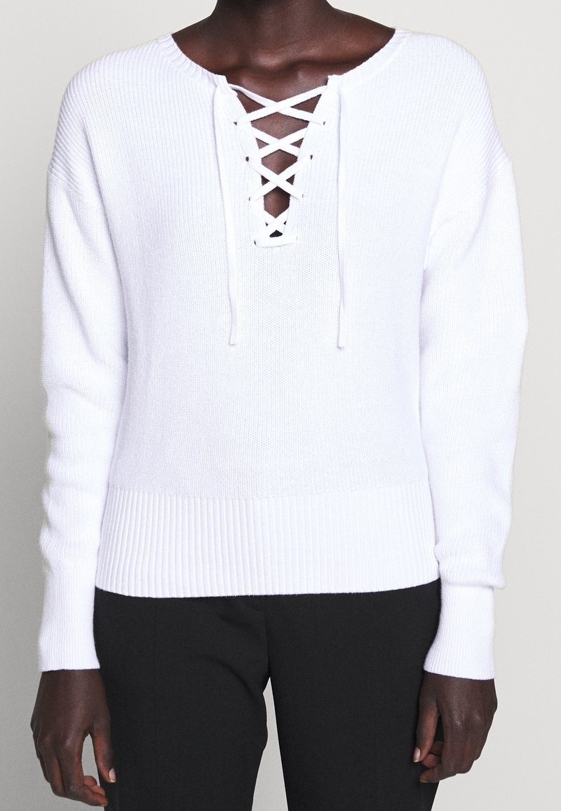 Maglione bianco lavorato a maglia con maniche lunghe, orlo a costine e dettagli con lacci sul collo. Texture morbida e vestibilità comoda.