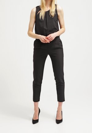Czarny bezrękawnik z zebranym dekoltem, charakteryzujący się prostą sylwetką, zwężanymi nogawkami i bocznymi kieszeniami, zestawiony z czarnymi szpilkami.