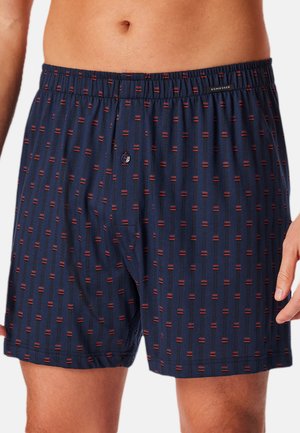 Boxer in blu navy con un motivo a righe verticali rosse e nere ripetute. Presenta una vita elasticizzata e una chiusura a pulsante sul fronte.