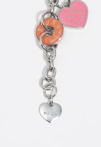 Cadena de metal plateado con tres charms: un charm en forma de dona naranja, un charm en forma de corazón rosa y un pequeño corazón plateado con grabado.