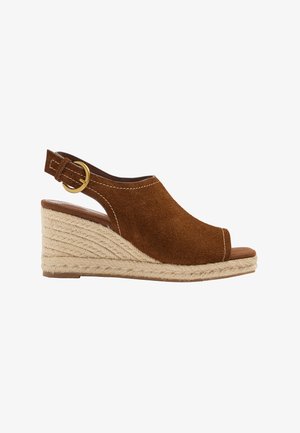Brązowy sandał na koturnie ze skóry zamszowej z odkrytym palcem, plecioną platformą z juty oraz regulowanym paskiem na kostkę ze złotą klamrą.