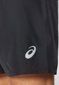 Pantalones cortos deportivos negros hechos de una tela suave y ligera, con un logo plateado en la parte inferior izquierda y costuras limpias y sencillas.