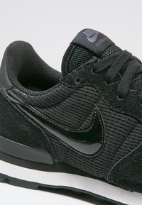 Svarta sneakers med ribbat tyg och överdel av mocka, glänsande accenter och en vit mellansula. Har perforeringar för ventilering och logotypdetalj.