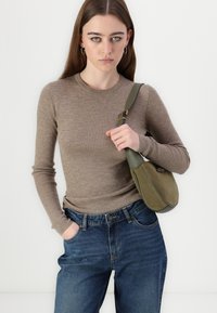 Béžová rebrovaná blúzka s dlhými rukávmi skombinovaná s tmavomodrými džínami so zvýšeným pásom. Olivovo zelená kabelka na rameno s oblým tvarom a zlatými akcentmi.