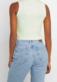 Débardeur à rayures vert clair avec un design court, associé à un jean en denim bleu clair taille haute avec poches arrière et passants de ceinture.