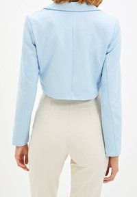 Blazer bleu clair court avec un col à revers et des manches longues, présentant un tissu lisse et un design épuré et ajusté.