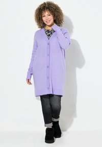 Cardigan long en lavande en tricot doux avec un devant à boutons, des poignets côtelés et une coupe décontractée, associé à un jean foncé et des bottes noires.