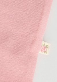 Helles rosa Gewebe mit weicher, glatter Textur; am Rand befindet sich ein kleines gewebtes Etikett mit floralem Design.