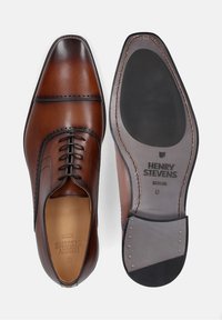 Scarpe eleganti in pelle marrone con un design elegante, presentano dettagli cuciti, punta arrotondata e una suola liscia con il marchio sulla parte inferiore.