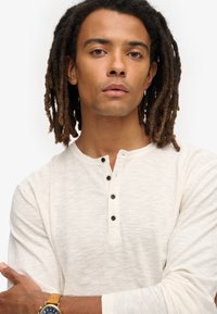 Lichtbeige langslavige henley-shirt gemaakt van textiel met structuur, met drie zwarte knopen en een ronde kraag.