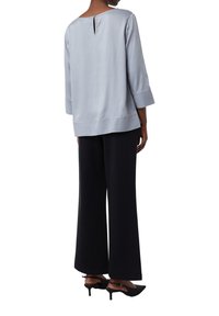 Top azzurro chiaro, morbido, a maniche lunghe con dettagli a chiave sul retro, abbinato a pantaloni neri larghi e tacchi neri. Design semplice e moderno.